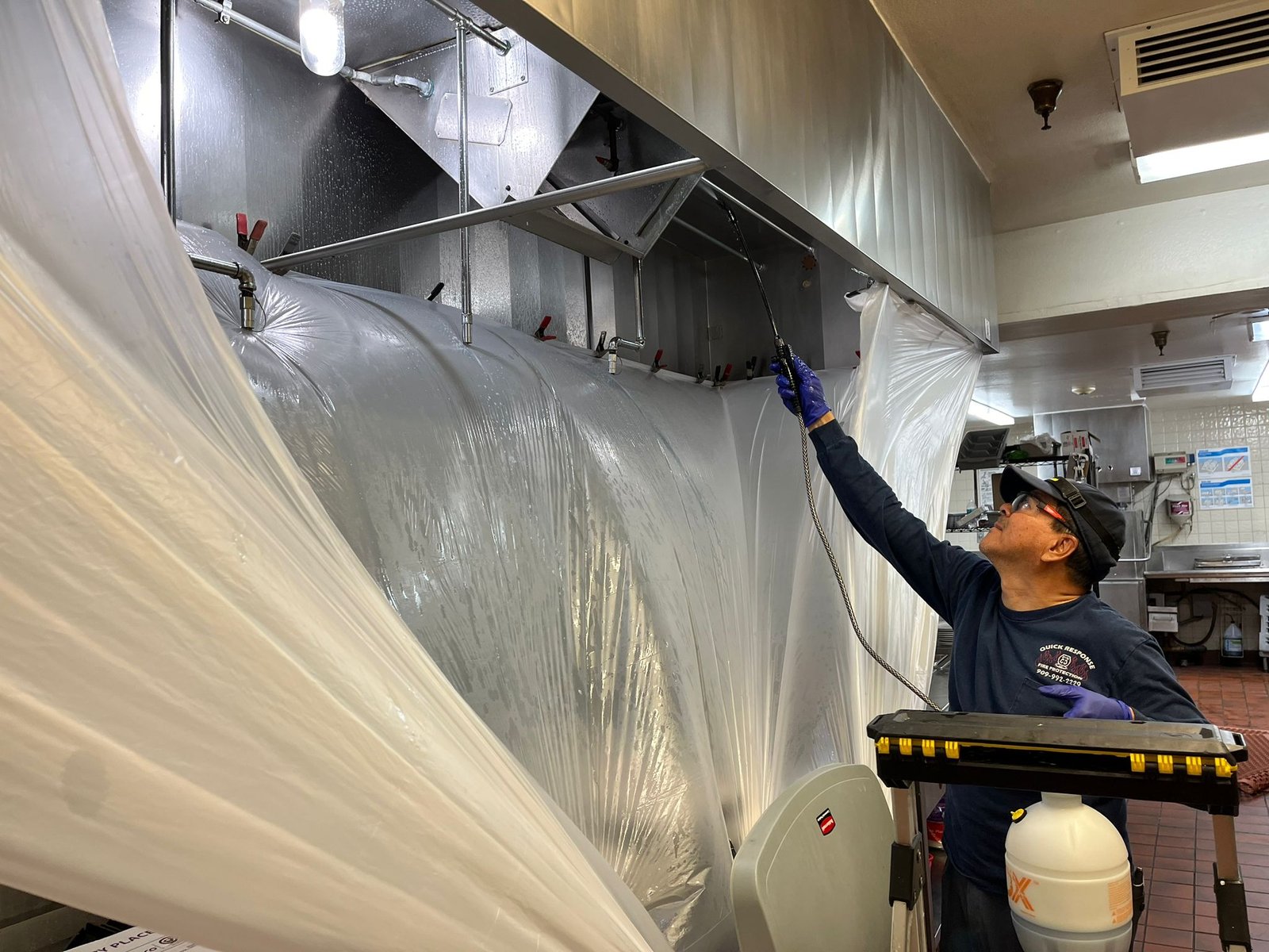 Technician cleaning a kitchen hood and exhaust system for fire prevention - Quick Response Fire Protection